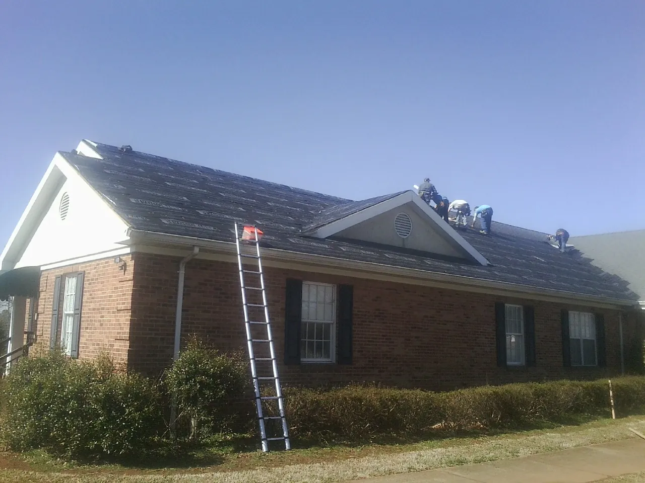 Crew tearing shingles off a brick ranch roof with a ladder set — Emergency Roof Repair work by our crew in Muscotah