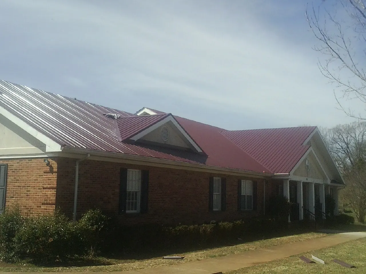 Red metal roof with gabled entries on a long brick building, from a Hail Damage Roof Repair job in Muscotah