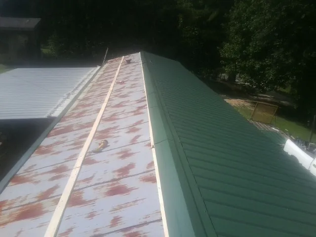 Old rusted panels beside newly installed green metal roofing — Wind Damage Roof Repair by Roofing Brothers in Muscotah