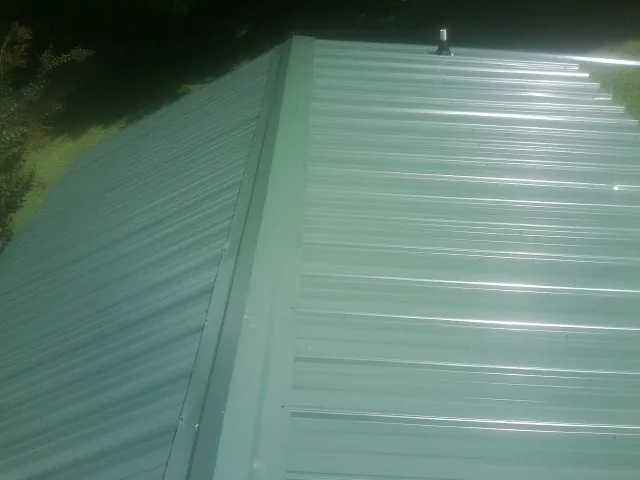 New green metal panels meeting at the ridge of a roof — Flat Roof Repair work by our crew in Muscotah