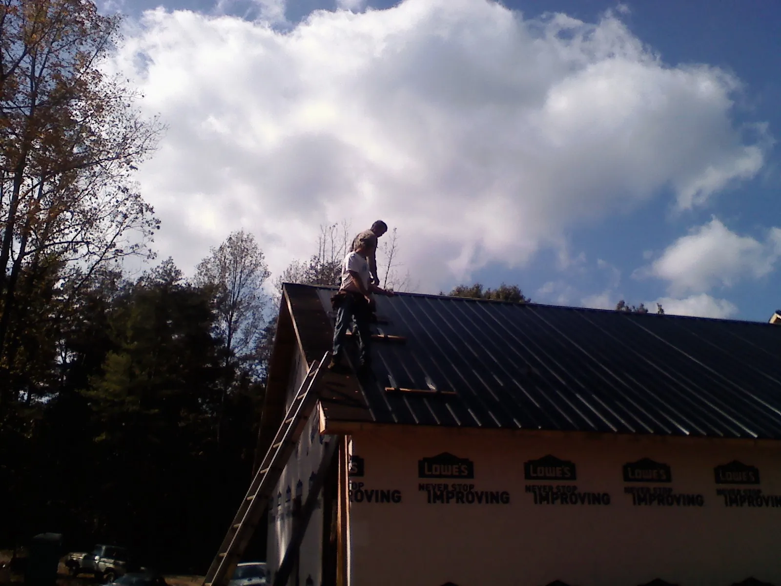 Roofer fastening dark metal panels high against a cloudy sky, from a Roof Inspection job in Muscotah