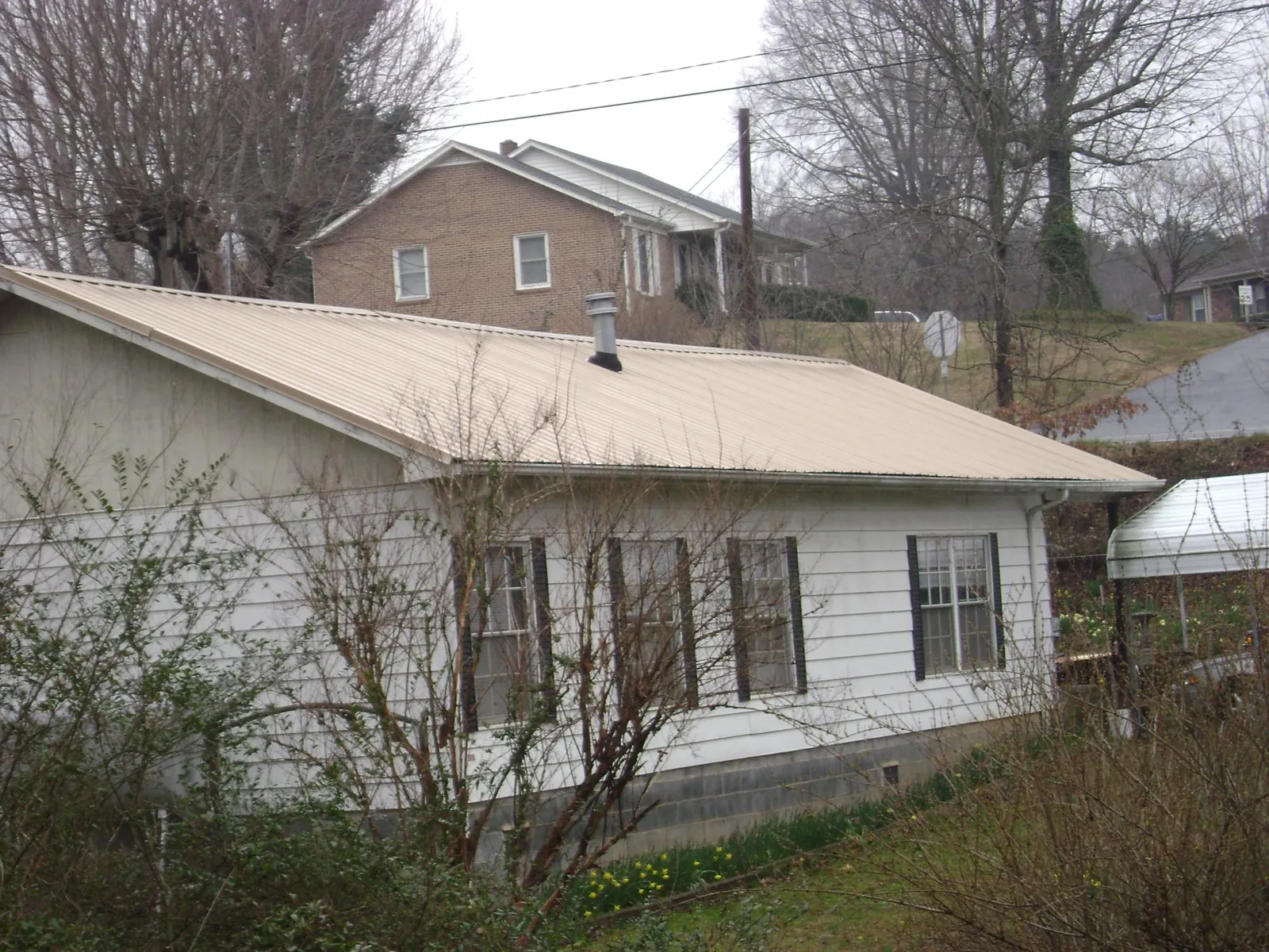 Tan metal roof on a white sided house set into a hillside — Commercial Roofing by Roofing Brothers in Muscotah